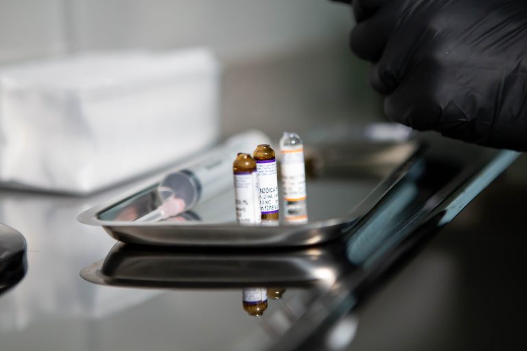 Close-up of medical vials and syringe on stainless tray in clinical setting.