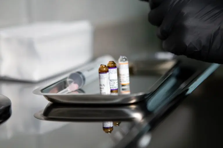 Close-up of medical vials and syringe on stainless tray in clinical setting.